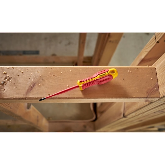 Tournevis isolé Stanley rouge et jaune posé sur une poutre en bois dans un atelier.
