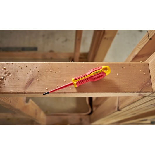 Tournevis isolé Stanley jaune et rouge posé sur une poutre en bois sur un chantier.