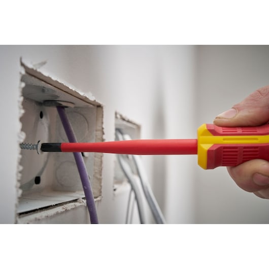 Main utilisant un tournevis isolé pour serrer une vis dans une boîte électrique avec des fils visibles.
