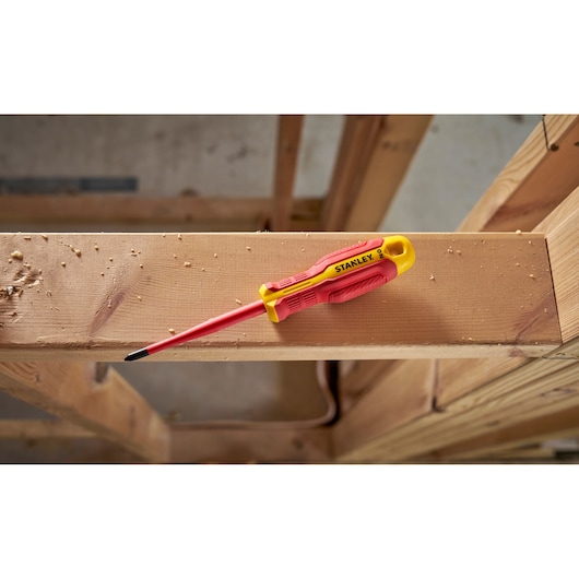 Tournevis isolé Stanley rouge et jaune posé sur une poutre en bois sur un chantier.