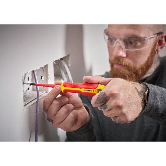 Personne utilise un tournevis STANLEY isolé pour travailler sur une prise électrique murale.