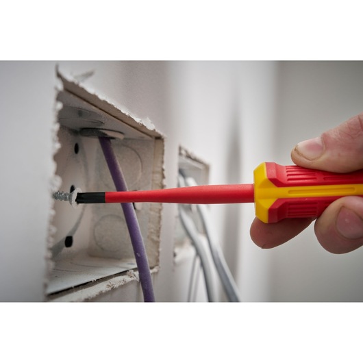Un tournevis isolé rouge et jaune est utilisé pour serrer une vis dans un boîtier mural électrique.