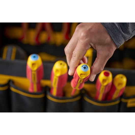 Une main prend un tournevis isolé jaune et rouge dans une trousse à outils avec d'autres outils visibles.