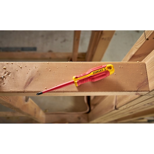 Tournevis isolé Stanley rouge et jaune posé sur une poutre en bois sur un chantier.