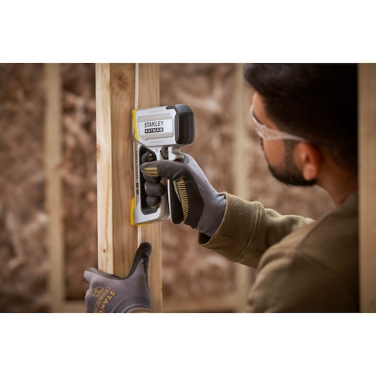 STANLEY FMHT70100-0 détecteur de montants tenu par une main gantée contre un cadre en bois sur un chantier.