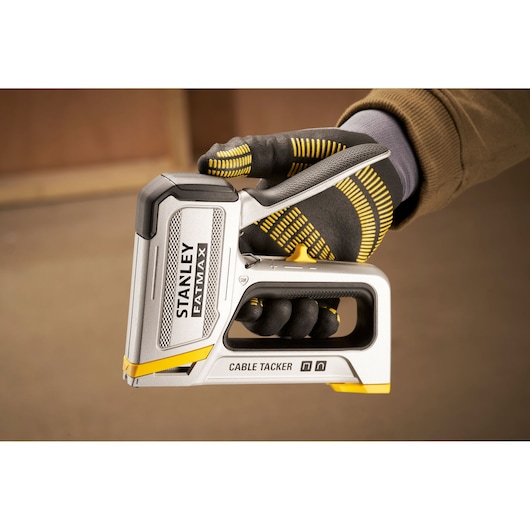 Agrafeuse de câbles Stanley FMHT70100-0 tenue en main gantée, argentée et jaune, vue latérale.