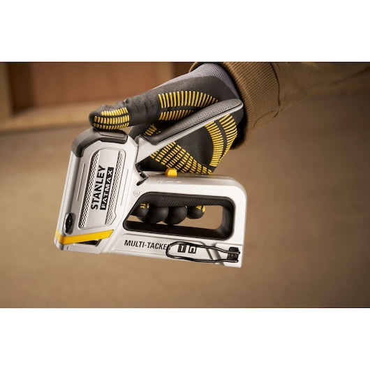 Photo de la pince à agrafes STANLEY FMHT70250-0 multi-tacker tenue dans une main gantée, vue latérale rapprochée.