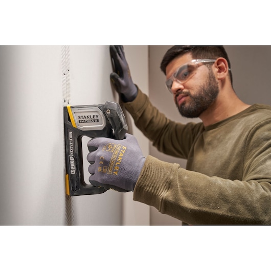 STANLEY FATMAX FMHT70401-0 multitacker utilisé sur cloison sèche par une personne avec des gants STANLEY, vue latérale.