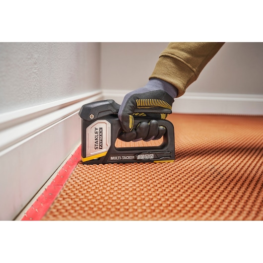 Photo de l'agrafeuse STANLEY FMHT70401-0 Multi-Tacker en utilisation, fixant la moquette près de la plinthe.