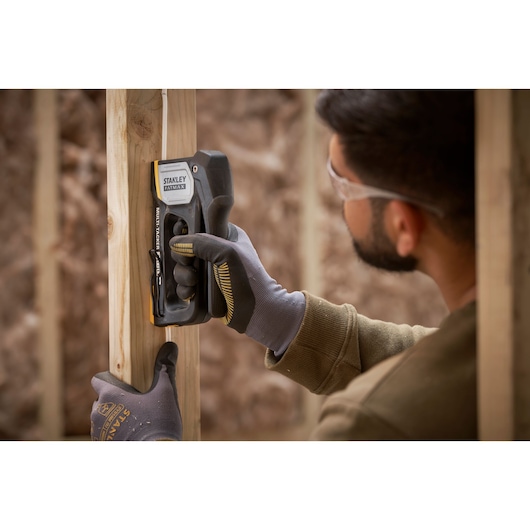 Agrafeuse STANLEY FMHT70401-0 utilisée par des mains gantées pour fixer un fil sur une structure en bois.