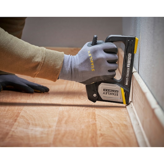 Agrafeuse multi-tacker STANLEY FMHT70401-0 utilisée pour fixer un revêtement près d'un mur, vue en gros plan.