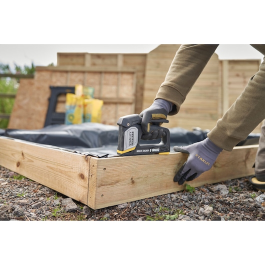 STANLEY FMHT70401-0 agrafeuse manuelle utilisée sur un cadre en bois à l'extérieur, gros plan sur des mains gantées.