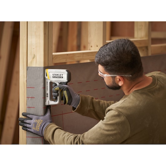 STANLEY FATMAX FMHT70443-0 agrafeuse utilisée par un ouvrier ganté fixant une feuille à une structure en bois.
