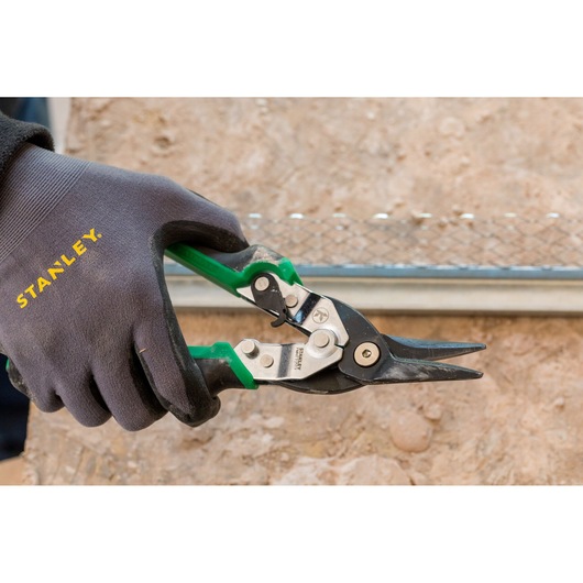 STANLEY FMHT73557-0 blikschaar met groene handgrepen vastgehouden door een gehandschoende hand, close-up foto.