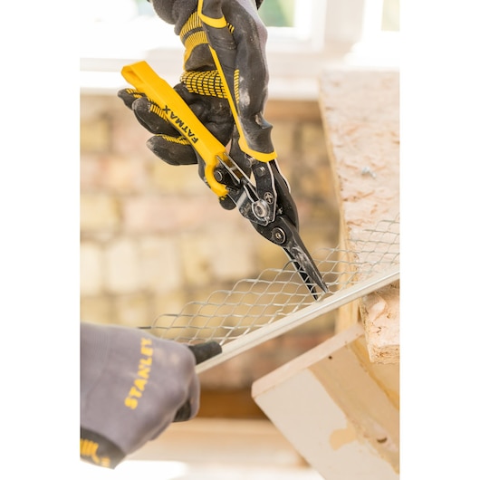 STANLEY FMHT73756-0 cisaille à tôle découpant un treillis métallique, gros plan, mains gantées en atelier.