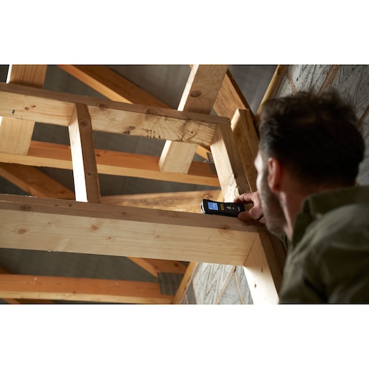 Télémètre laser STANLEY FMHT77165-0 utilisé par une personne pour mesurer une poutre en bois sur un chantier.