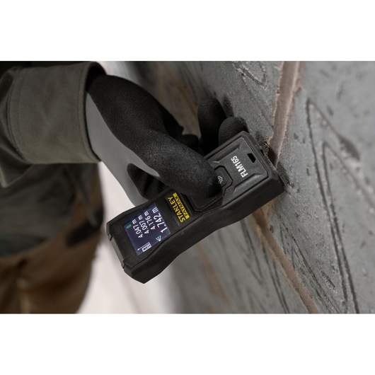 Stanley FMHT77165-0 télémètre laser tenu contre un mur par une main gantée, vue rapprochée.