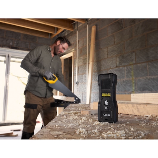 Photo du télémètre laser STANLEY FMHT77165-0 sur établi avec sciure dans un environnement de construction.