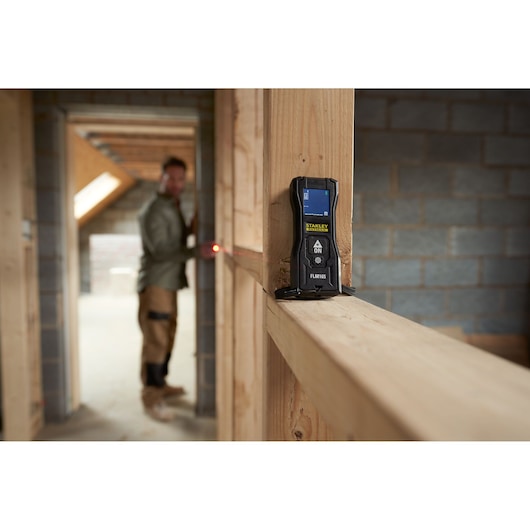 STANLEY FMHT77165-0 télémètre laser utilisé sur une charpente en bois, environnement de construction.