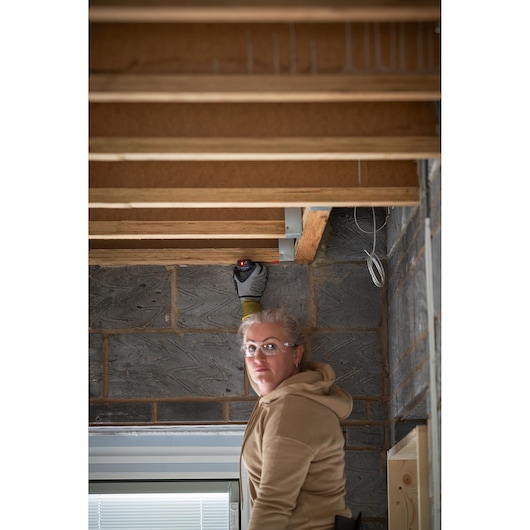 Photographie du télémètre laser STANLEY FMHT77165-0 utilisé sur des poutres de plafond en bois lors d’un chantier.