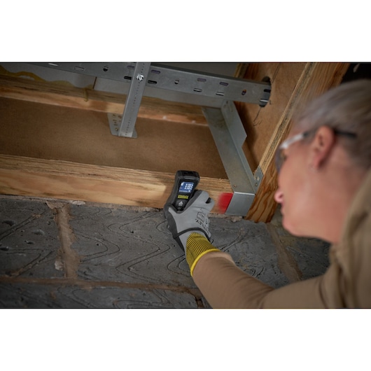 STANLEY FMHT77165-0 télémètre laser utilisé sur une poutre en bois, utilisateur avec gants de sécurité.
