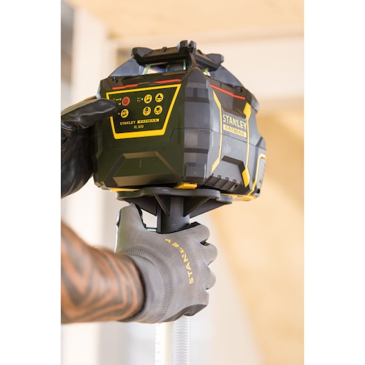 Photo du niveau laser rotatif STANLEY FMHT77446-1 utilisé par une main gantée sur un chantier.