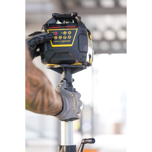 Photo du niveau laser rotatif STANLEY FMHT77447-1 utilisé par une main gantée, produit en utilisation extérieure.