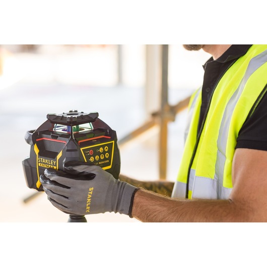Photo du niveau laser STANLEY FMHT77447-1 tenu par un ouvrier avec gilet de sécurité et gants.
