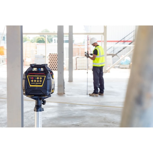STANLEY FMHT77447-1 niveau laser rotatif sur trépied, chantier en arrière-plan, ouvrier mesurant.