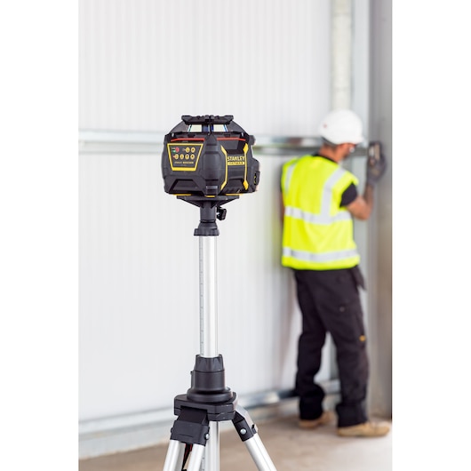 Laser rotatif STANLEY FMHT77447-1 sur trépied, ouvrier flou en équipement de sécurité en arrière-plan.