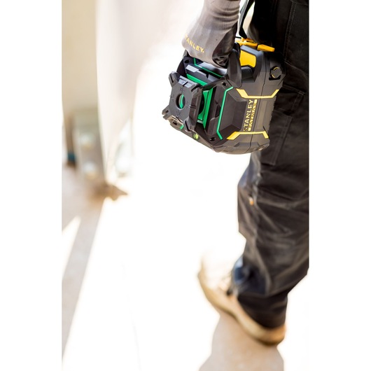 Niveau laser STANLEY FMHT77448-1 tenu par un ouvrier en pantalon noir et gants, en extérieur.