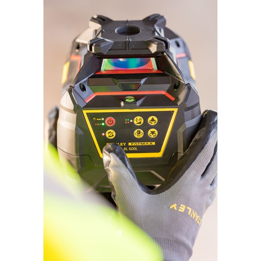 Photo du niveau laser rotatif STANLEY FMHT77449-1 tenu par des mains gantées, gros plan sur le panneau de commande.