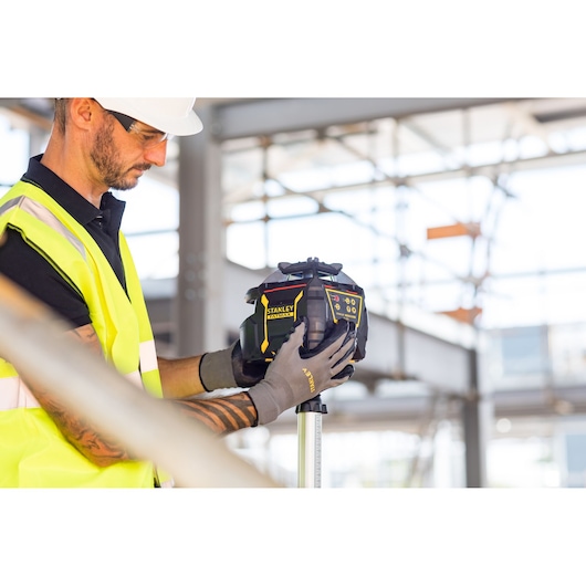 STANLEY FMHT77449-1 niveau laser tenu par un ouvrier en gilet haute visibilité sur chantier.