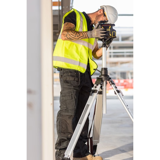 Niveau laser de chantier STANLEY FMHT77449-1 sur trépied, utilisé par ouvrier avec gilet et casque.