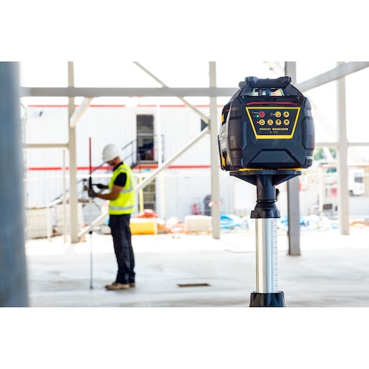 STANLEY FMHT77449-1 niveau laser rotatif sur trépied sur chantier, ouvrier en arrière-plan.
