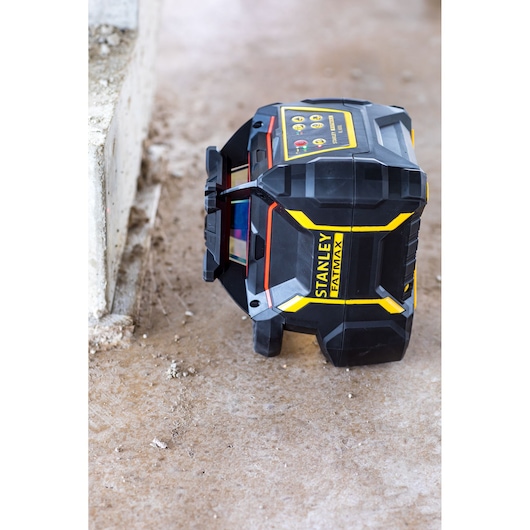 Niveau laser STANLEY FMHT77449-1 sur sol en béton, vue en angle, boîtier noir et jaune.