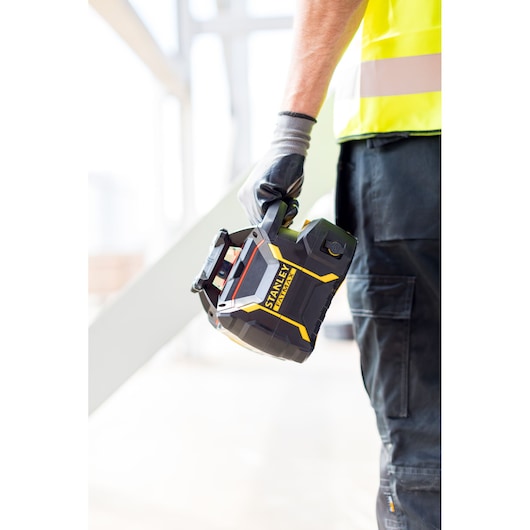 Niveau laser STANLEY FMHT77449-1 noir et jaune, tenu par un ouvrier avec des gants et un gilet de sécurité.
