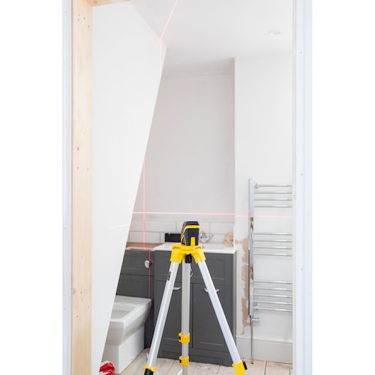 STANLEY FMHT77585-1 laserwaterpas op statief in badkamer, projecteert rode horizontale en verticale lijnen.