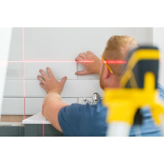 STANLEY FMHT77585-1 laser waterpas gebruikt bij tegelwand, close-up met rode laserlijnen en handen.
