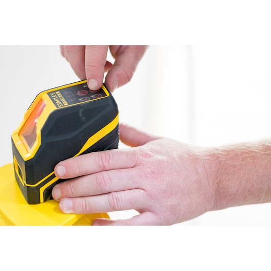STANLEY FMHT77585-1 laser waterpas in gebruik, close-up van hand op bedieningstoetsen.