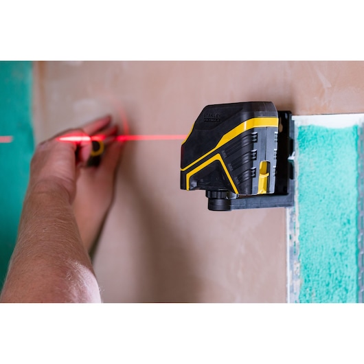 STANLEY FMHT77585-1 laser waterpas projecteert een rode lijn op de muur, gebruikt met de hand, zijaanzicht.