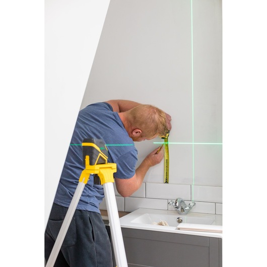 STANLEY FMHT77586-1 laserwaterpas op statief projecteert groene lijnen terwijl man de muur in de badkamer meet.
