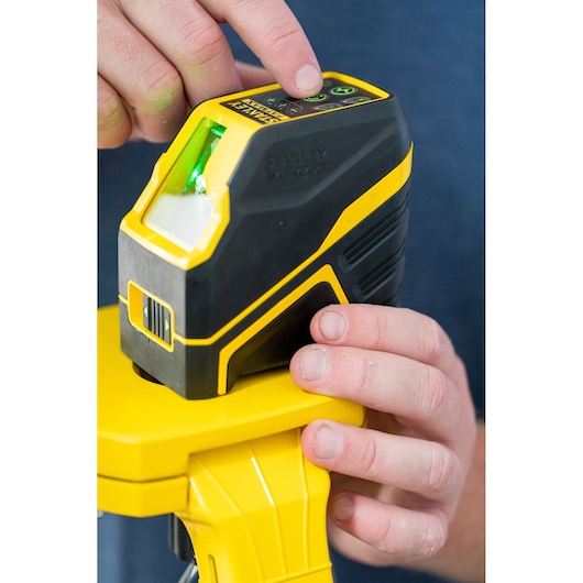 STANLEY FMHT77586-1 kruislijnlaser met groene straal op statief, close-up van handen die de bovenste knoppen bedienen.