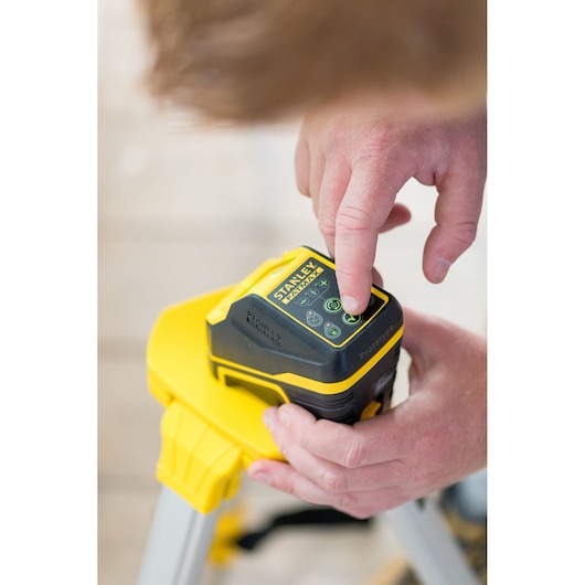 STANLEY FMHT77586-1 laserwaterpas op statief, gebruiker drukt op bedieningspaneel, close-up weergave.