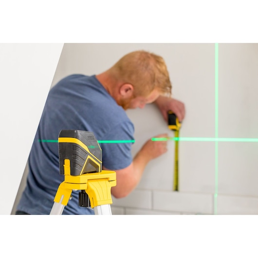 STANLEY FMHT77586-1 laserwaterpas op statief met groene lijnen, persoon meet muur.