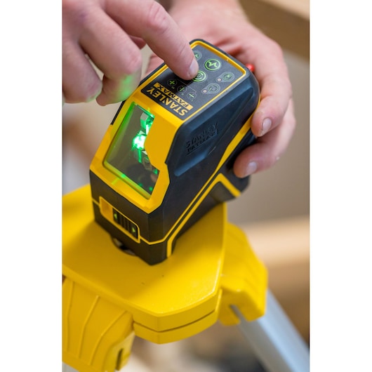 STANLEY FMHT77595-1 laserwaterpas op statief, close-up van hand op bedieningsknoppen met groene laser aan.
