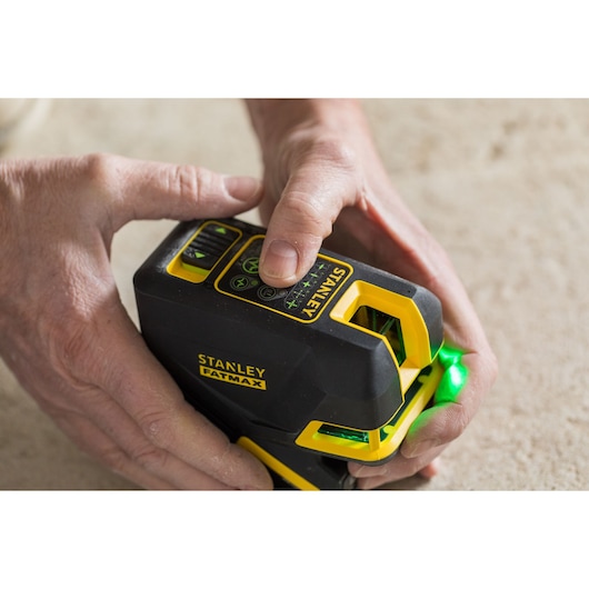 Foto van STANLEY FMHT77598-1 laserwaterpas, zwart en geel, vastgehouden door handen, groen licht geactiveerd.
