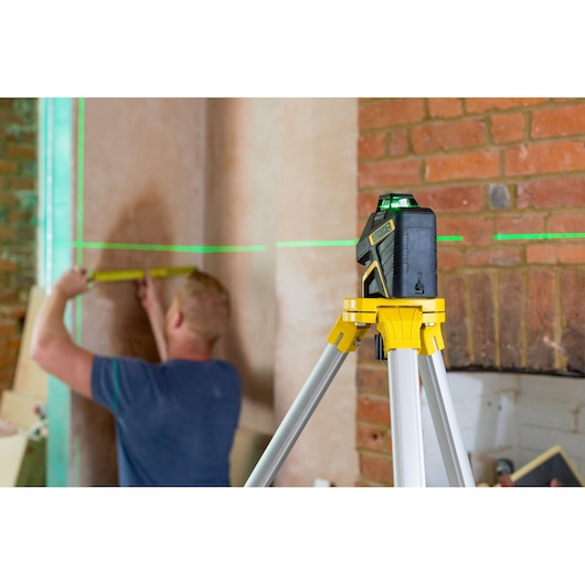 STANLEY FMHT77617-1 laserwaterpas op statief projecteert groene lijnen terwijl iemand een muur opmeet.
