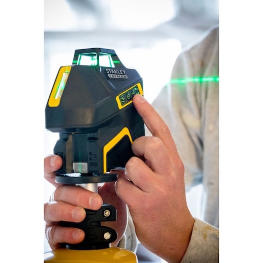 Foto van STANLEY FMHT77617-1 laserwaterpas, bediend door een hand, met verlicht bedieningspaneel en groene laserlijn.