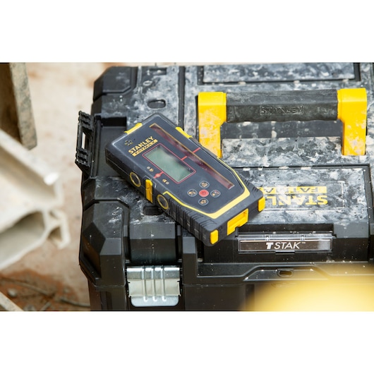 Télémètre laser STANLEY FMHT77652-0 noir et jaune posé sur boîte à outils, vue de dessus en angle.